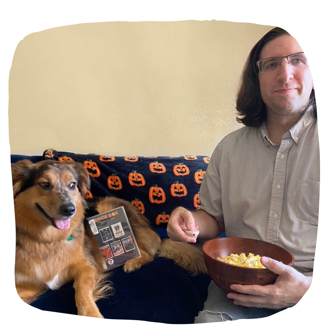 A man sitting next to a dog holding a bowl of popcorn and a dvd player remote 